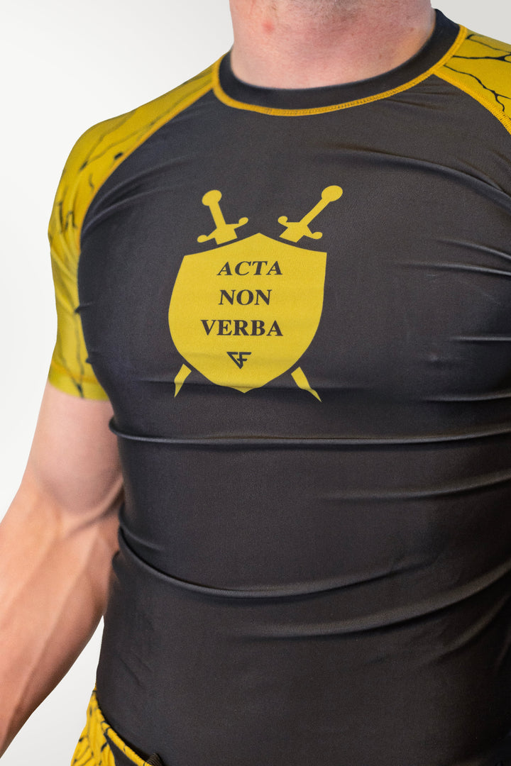 Person wearing a black and yellow athletic shirt with 'Acta Non Verba' design.